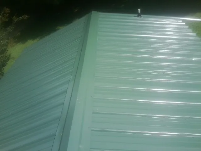 New green metal panels meeting at the ridge of a roof — Flat Roof Repair work by our crew in Clayton