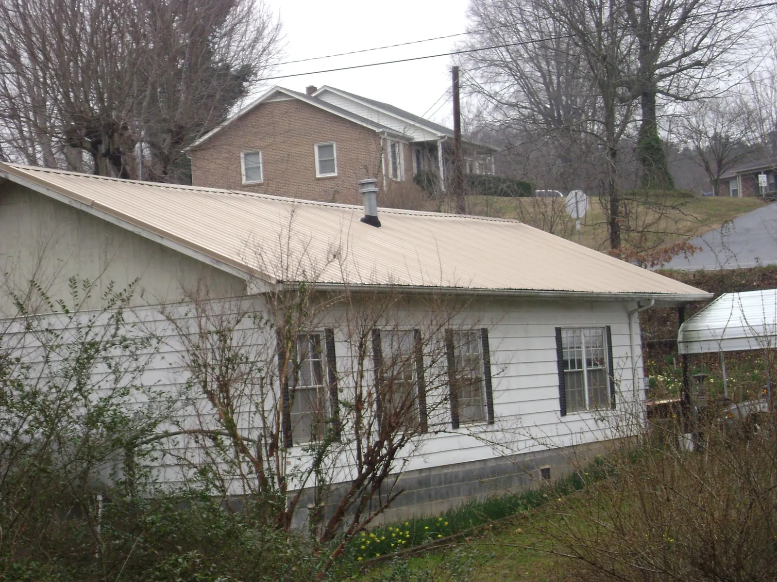 Tan metal roof on a white sided house set into a hillside — Commercial Roofing by Roofing Brothers in Clayton